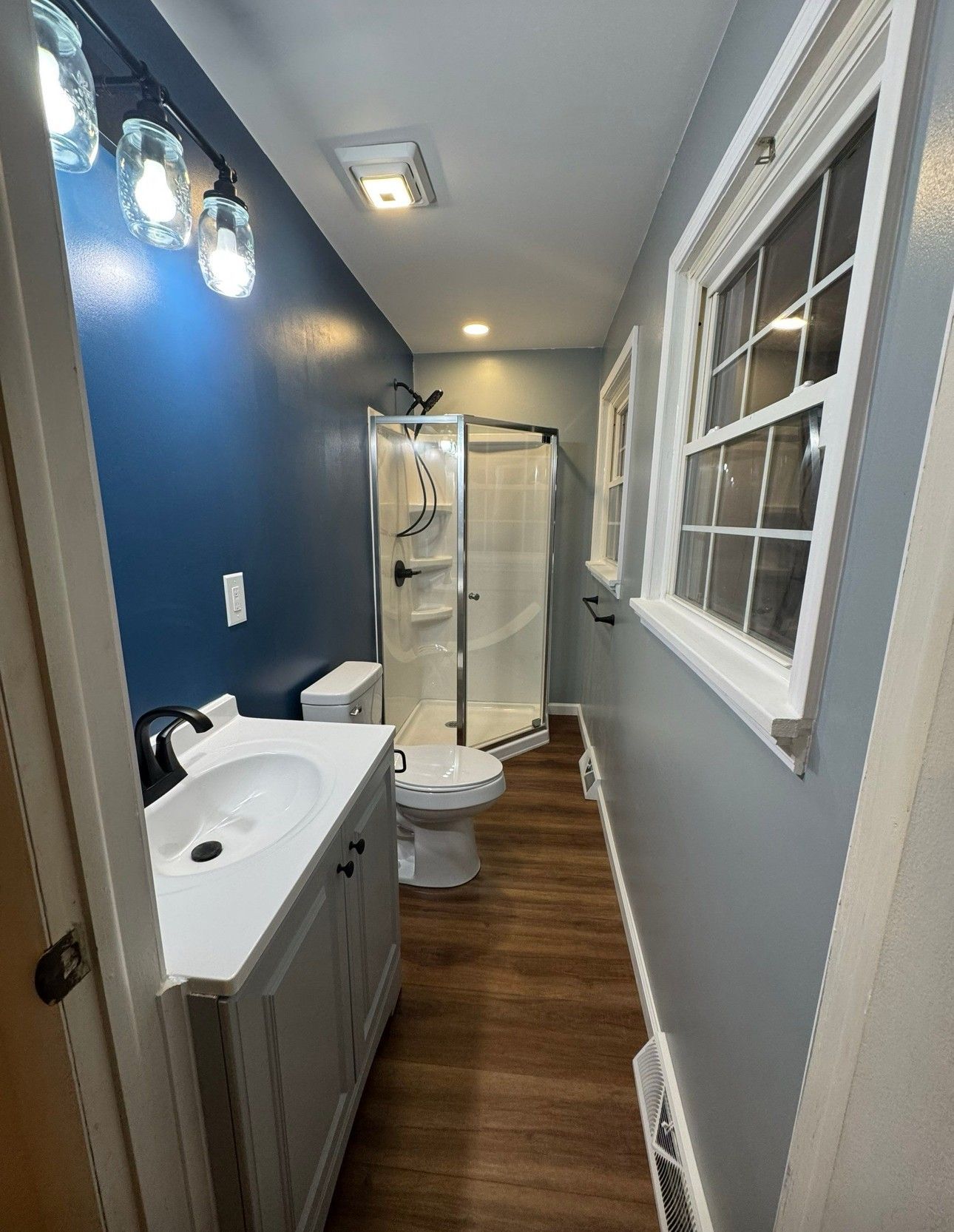 Bathroom with blue accent wall, white vanity, shower, toilet, and window.