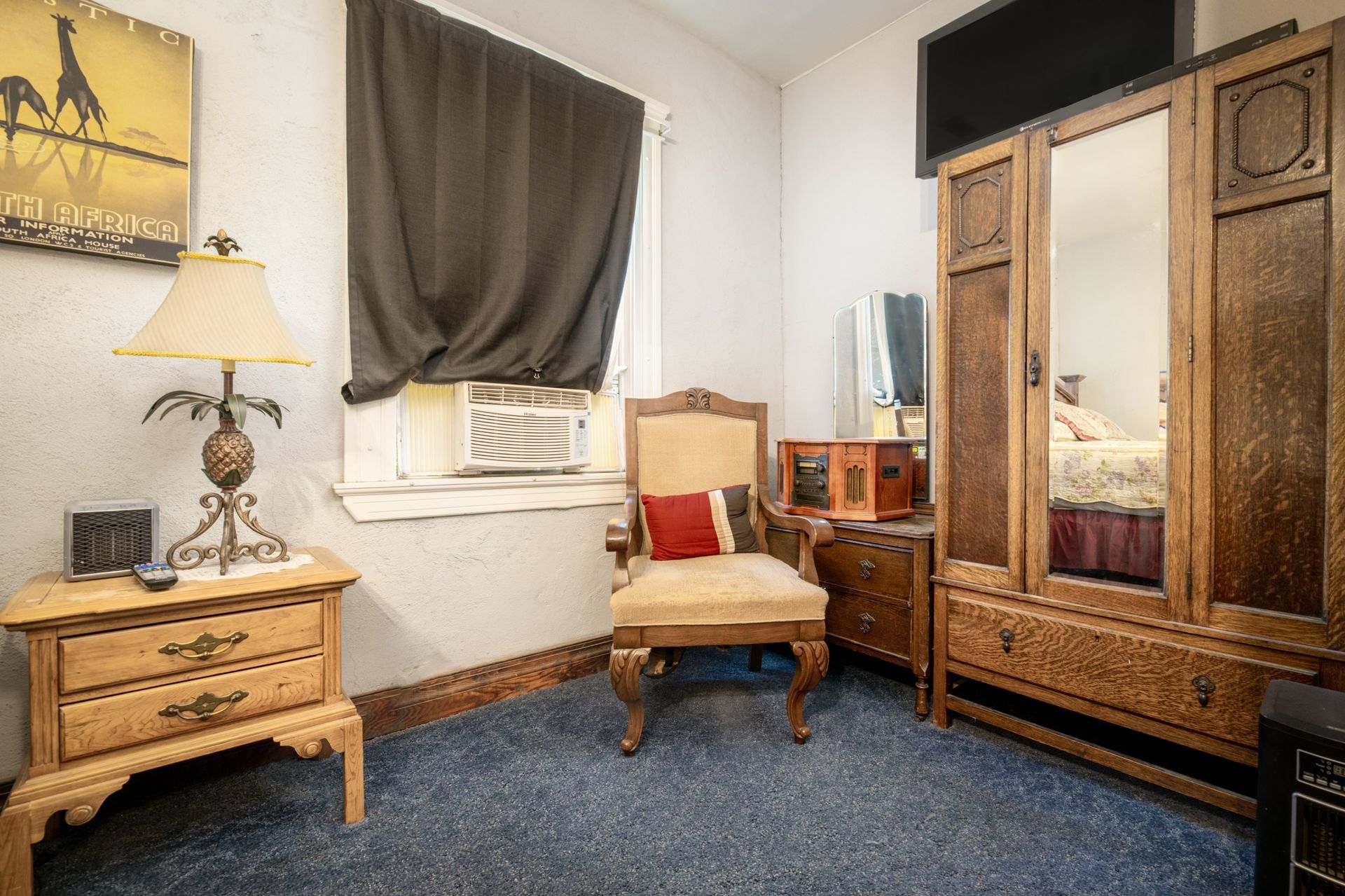 A bedroom with a chair , nightstand , wardrobe , and mirror.
