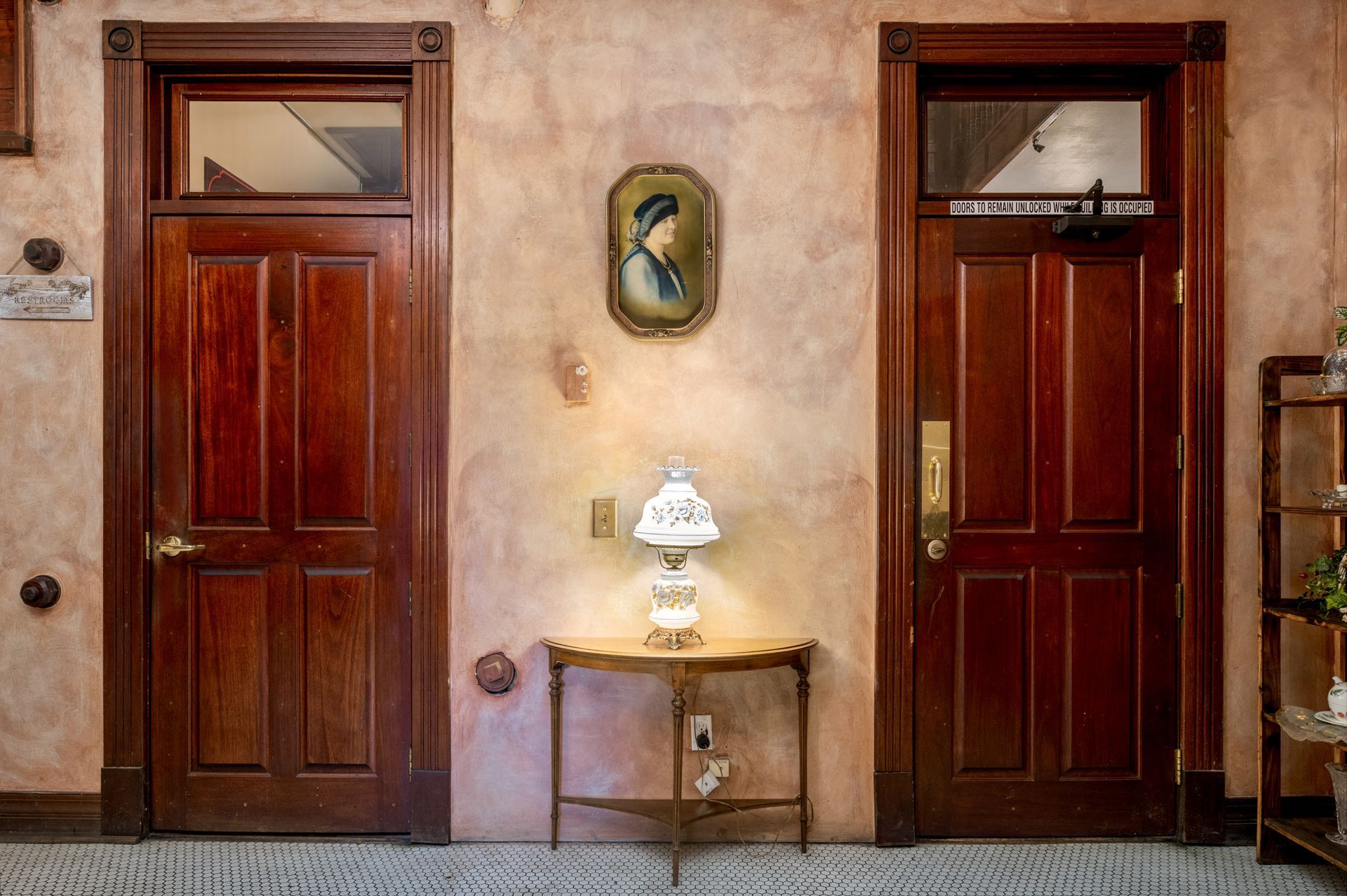 A hallway with two wooden doors and a table with a lamp on it.