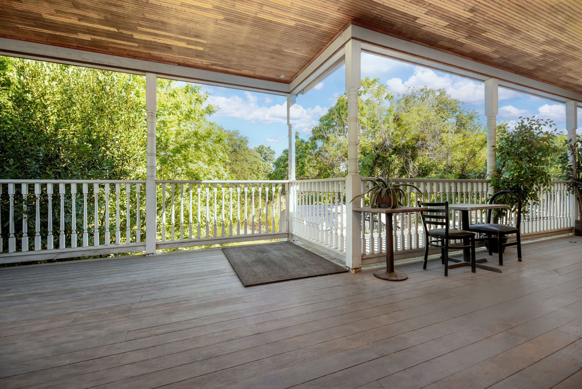 An empty porch with a table and chairs and trees in the background