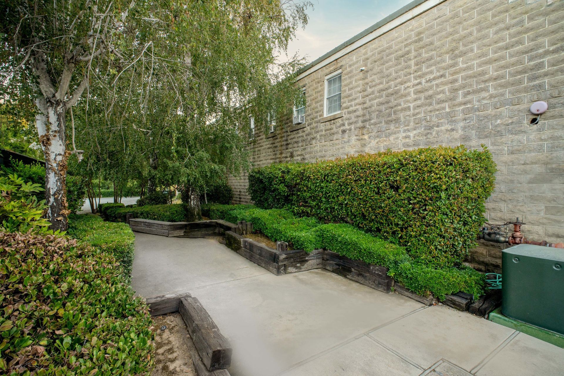 A brick building with a concrete walkway leading to it surrounded by trees and bushes.