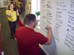 A man in a red shirt is writing on a white board.