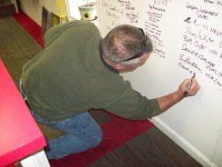 A man is kneeling down writing on a whiteboard.