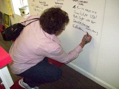A woman in a pink shirt is writing on a whiteboard.