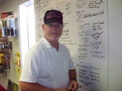 A man wearing a hat is standing in front of a white board.