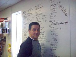 A man is standing in front of a white board with writing on it.
