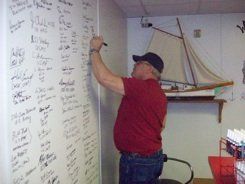 A man in a red shirt is writing on a whiteboard.
