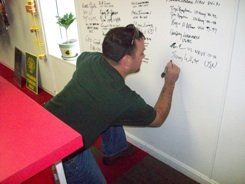 A man in a green shirt is writing on a white board.