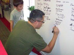 A man is writing on a whiteboard while a boy watches.