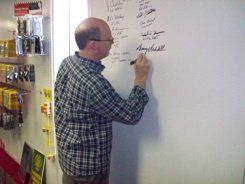 A man in a plaid shirt is writing on a whiteboard.