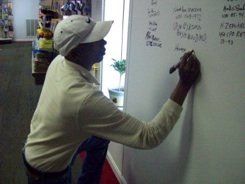 A man in a white hat is writing on a white board