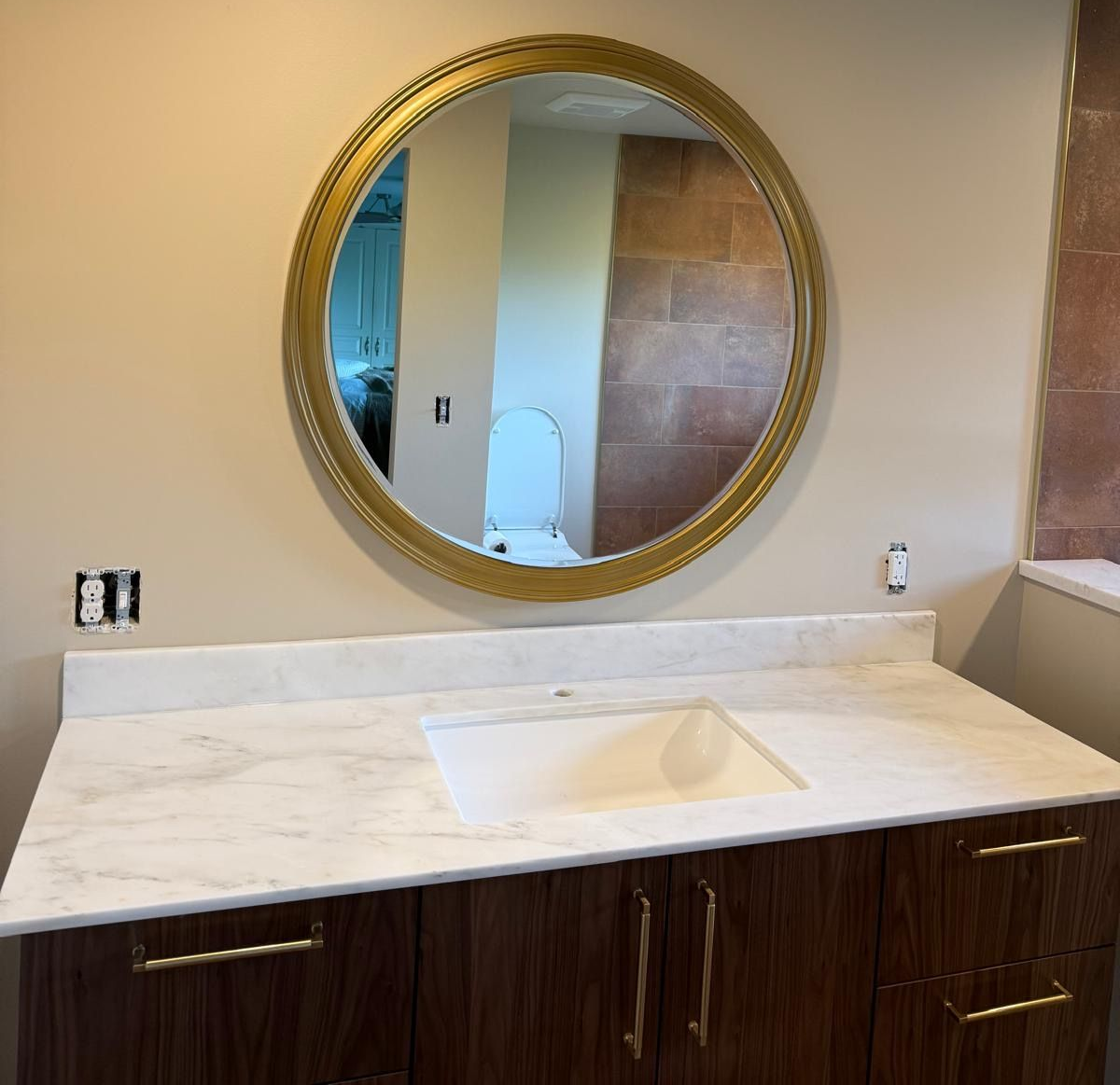 Bright bathroom vanity with granite countertop, dark wood cabinets, gold fixtures, and large mirror by a window Bright bathroom vanity with granite countertop, dark wood cabinets, gold fixtures, and large mirror by a window