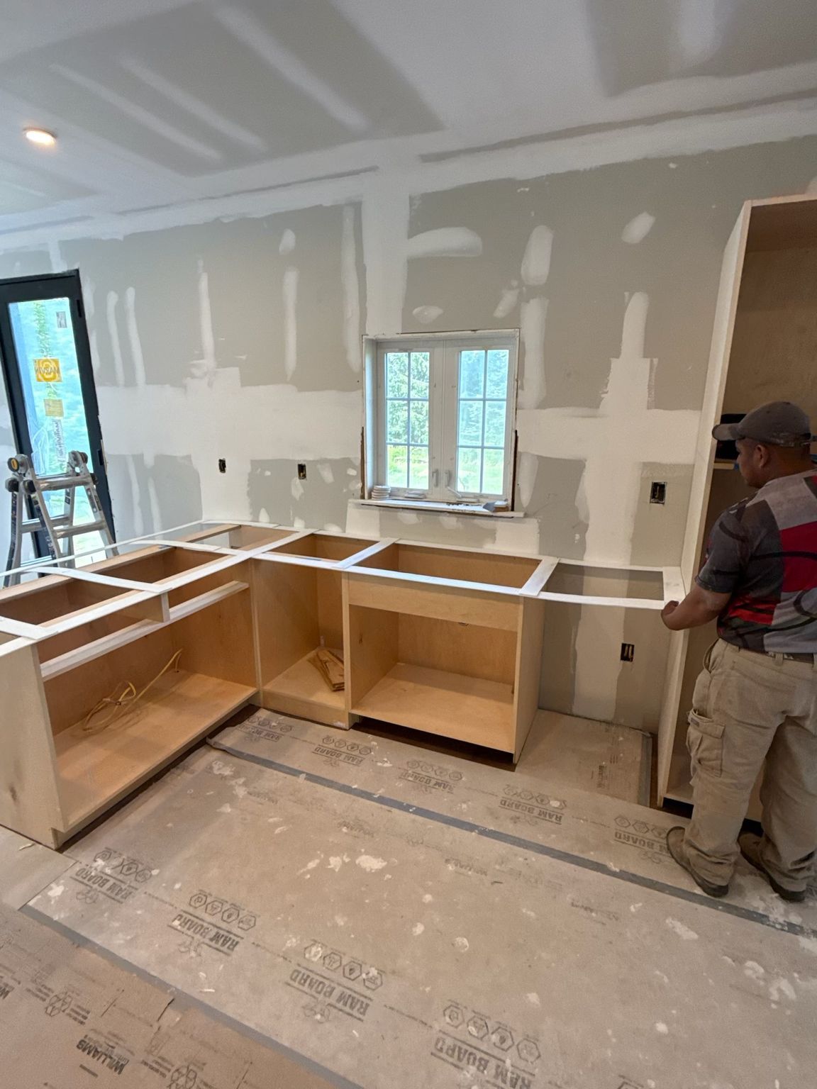 Partially built kitchen with unfinished cabinets, drywall, and a worker near the doorway