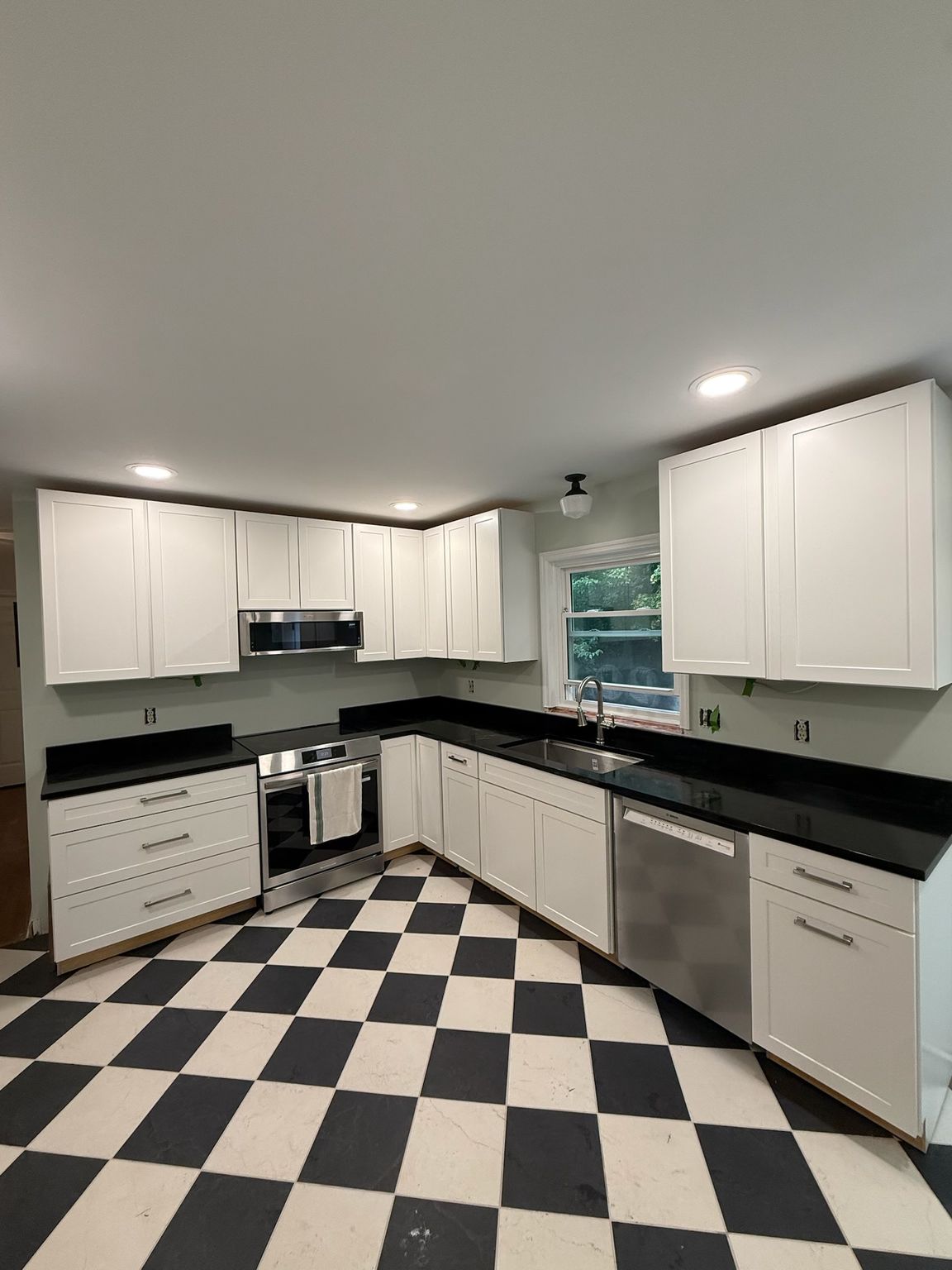 Bright white kitchen with black countertops and a black-and-white checkered floor, stainless appliances.