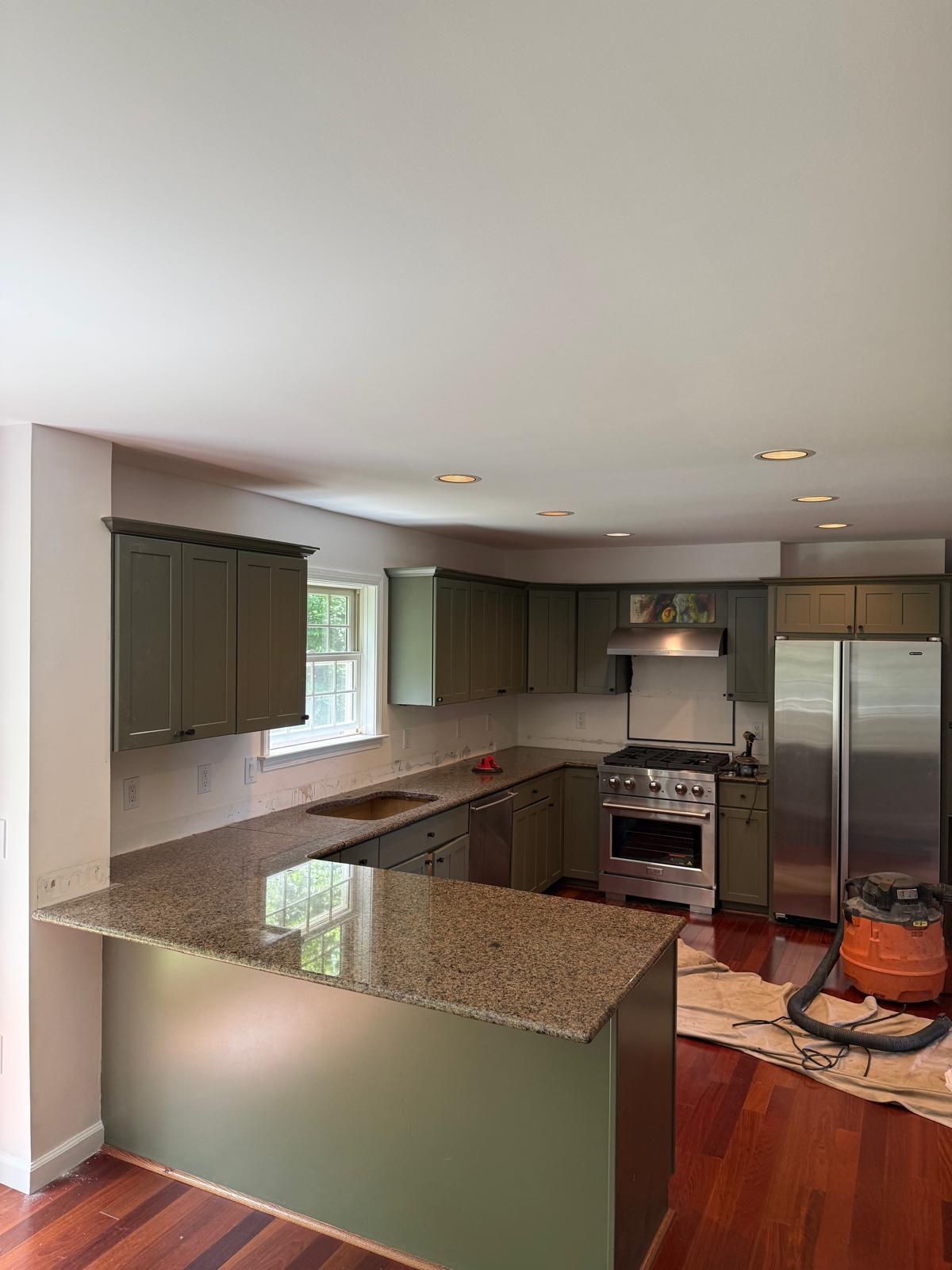 Small kitchen under renovation with white cabinets, black-and-white tile floor, and covered floor area.