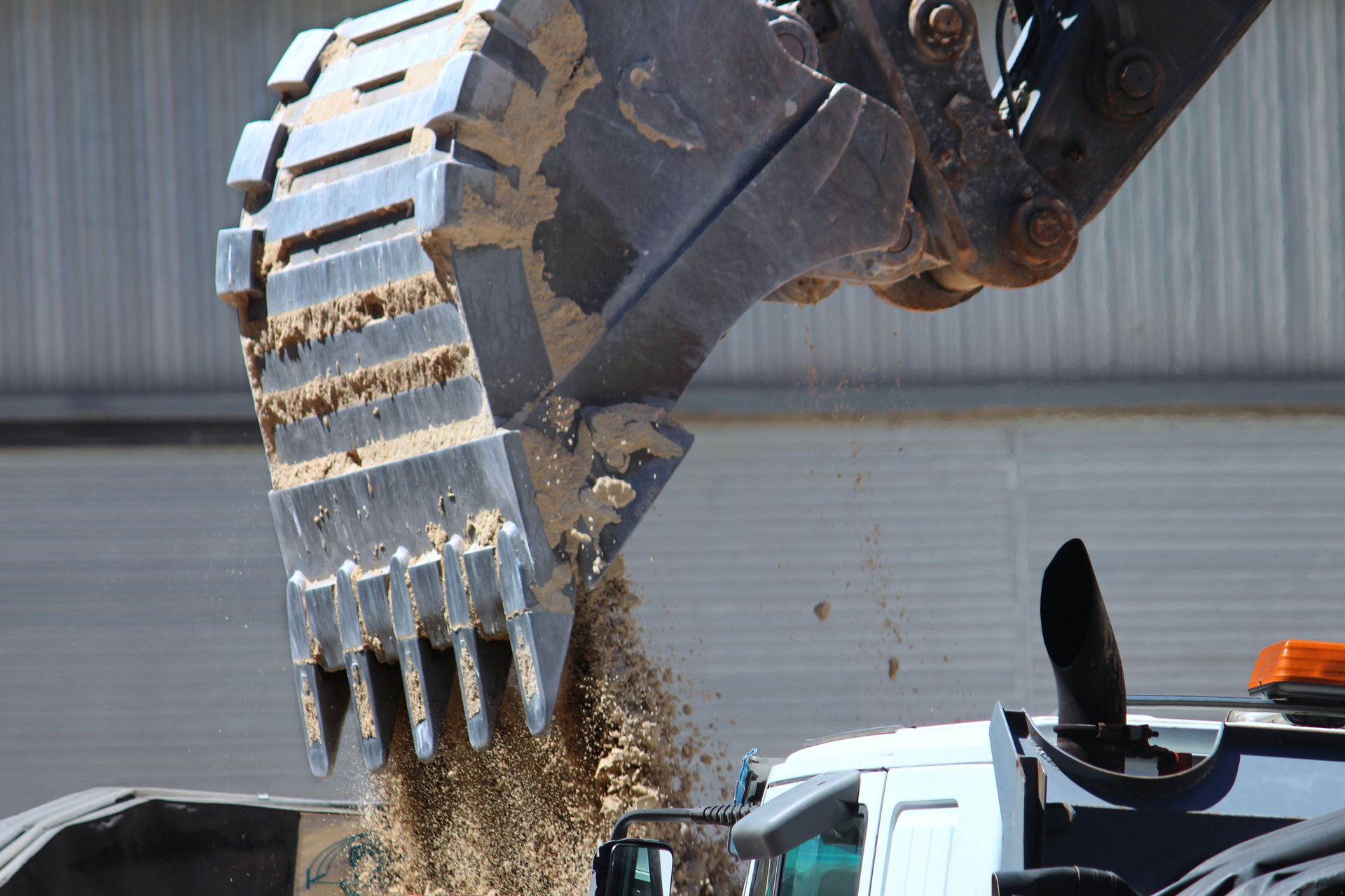 An excavator bucket unloading soil into a truck at a construction site. An excavator bucket unloading soil into a truck at a construction site.