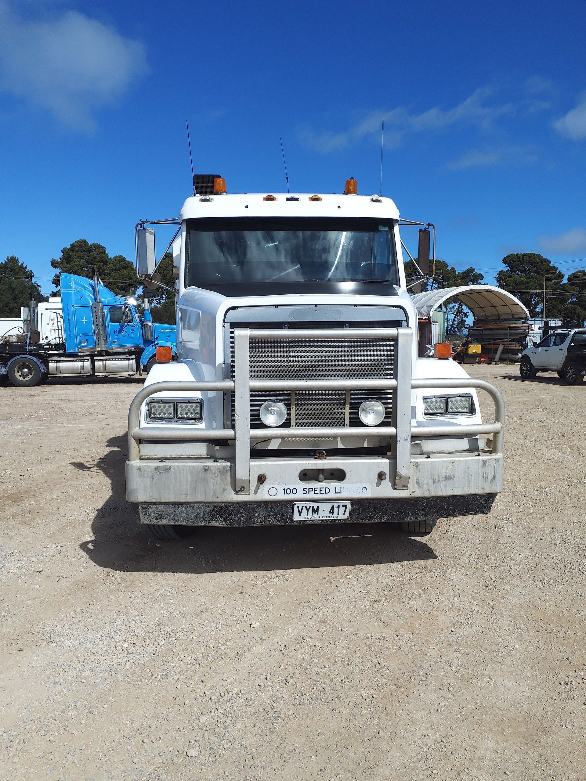 White truck with a front guard on a gravel lot under a blue sky.