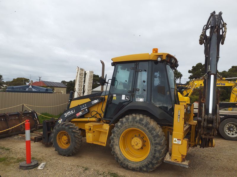 Yellow backhoe with raised backhoe arm; parked outside.