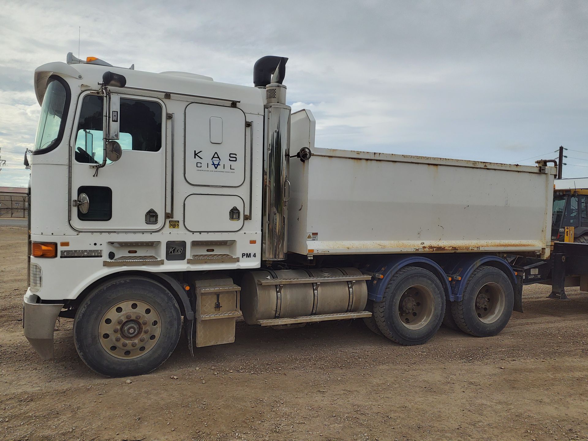 White dump truck parked on dirt, cloudy sky background.