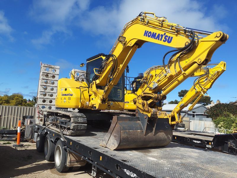 Yellow Komatsu excavator on a flatbed trailer, under a blue sky, ready for transport.