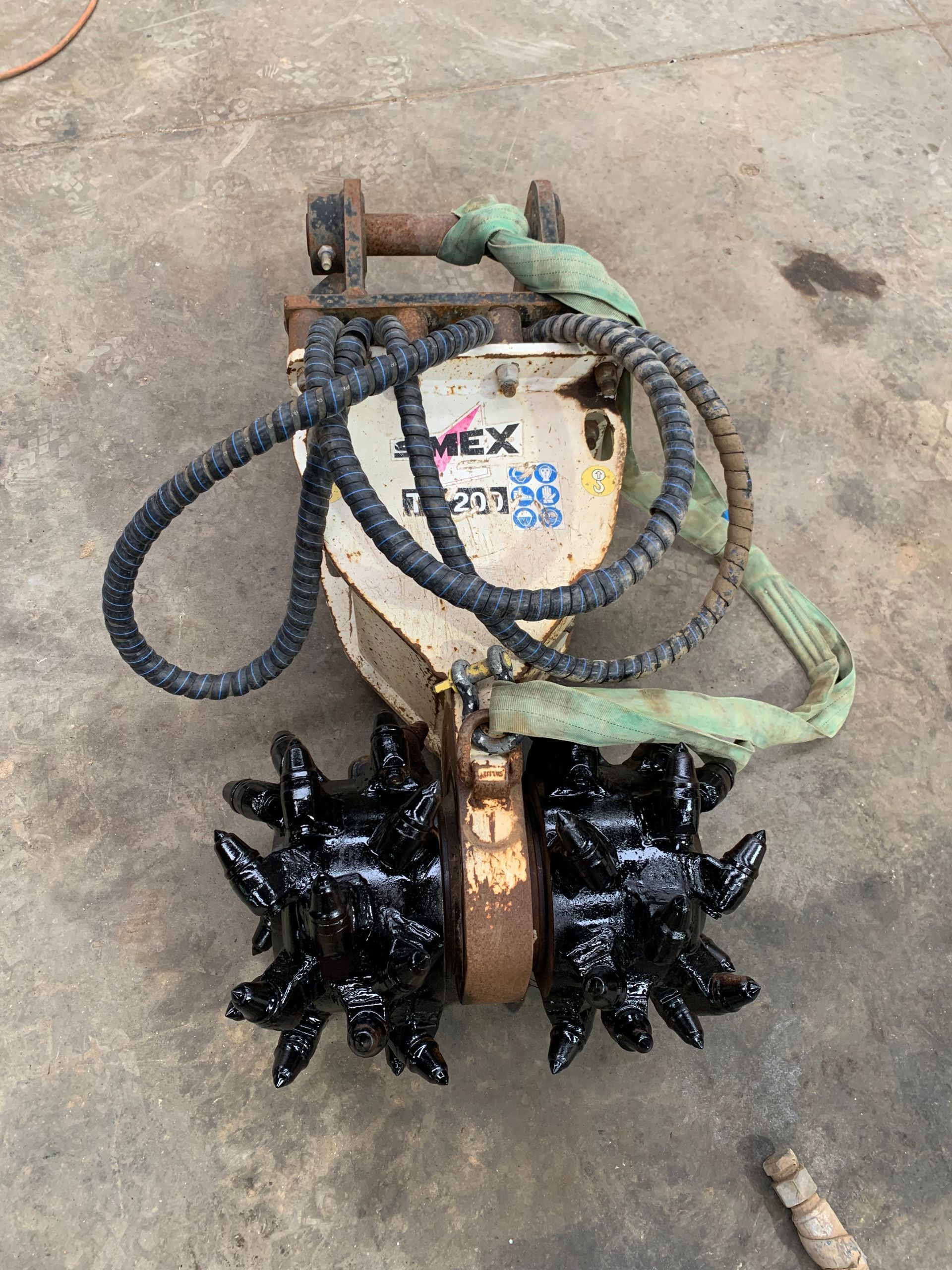 Excavator attachment with two spiked wheels, beige and black, resting on concrete.