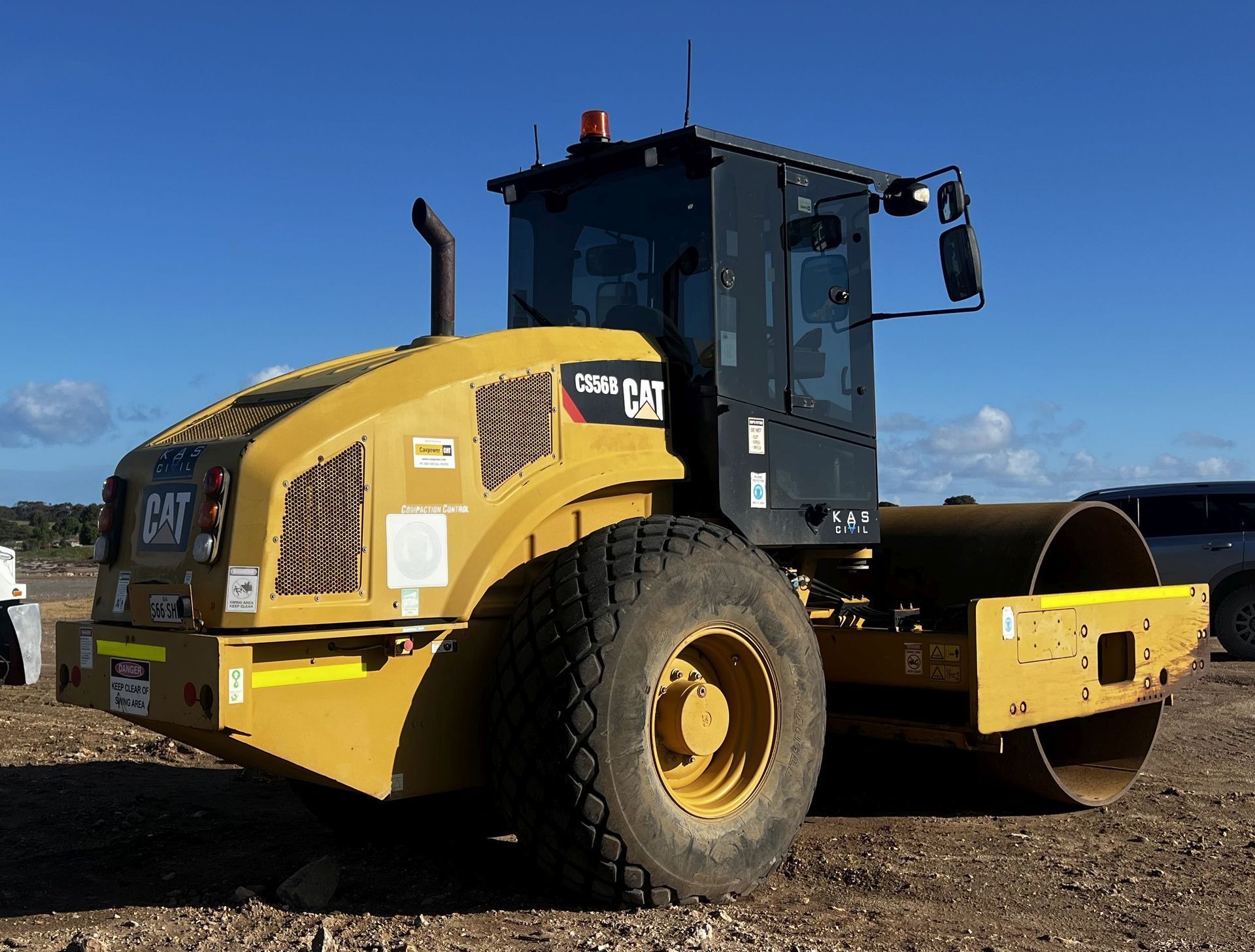 Yellow Caterpillar compactor on a construction site; blue sky.