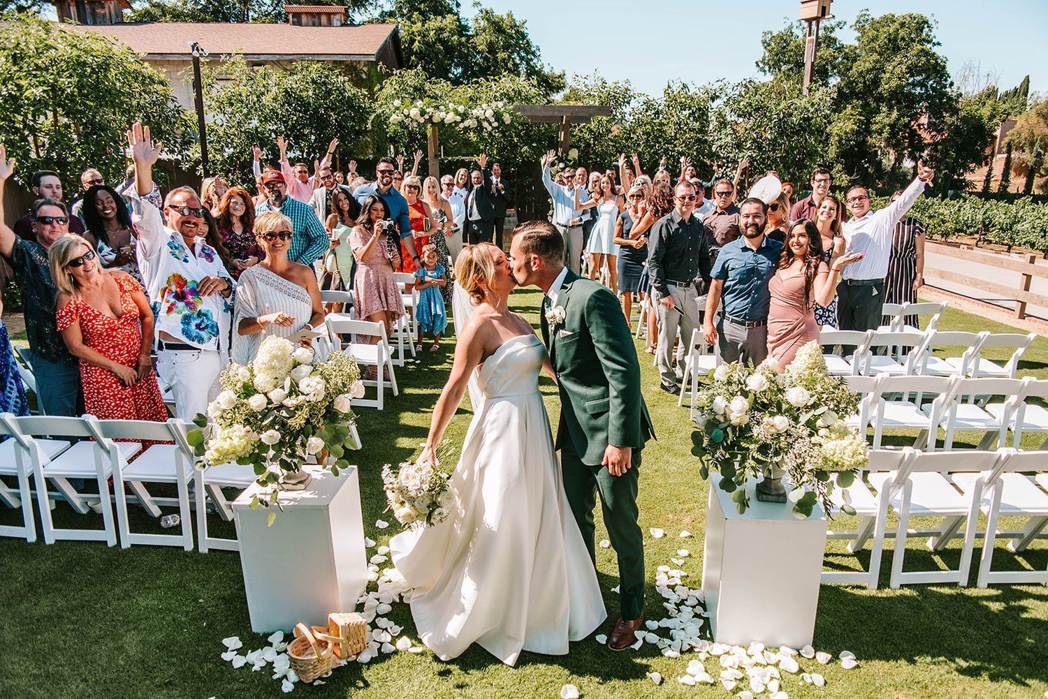 A bride and groom are kissing in front of their wedding guests.