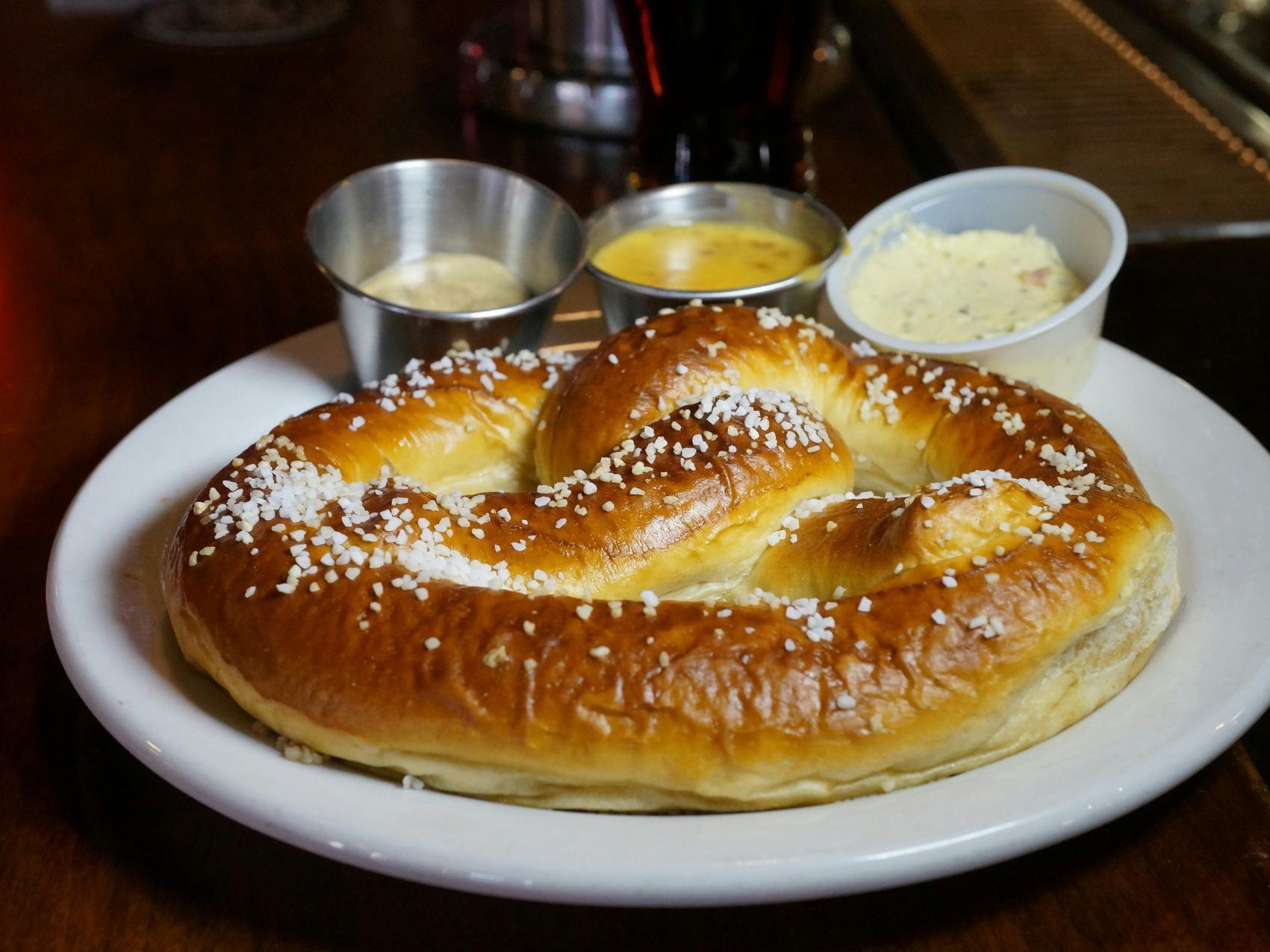 A pretzel is on a white plate with dipping sauces.