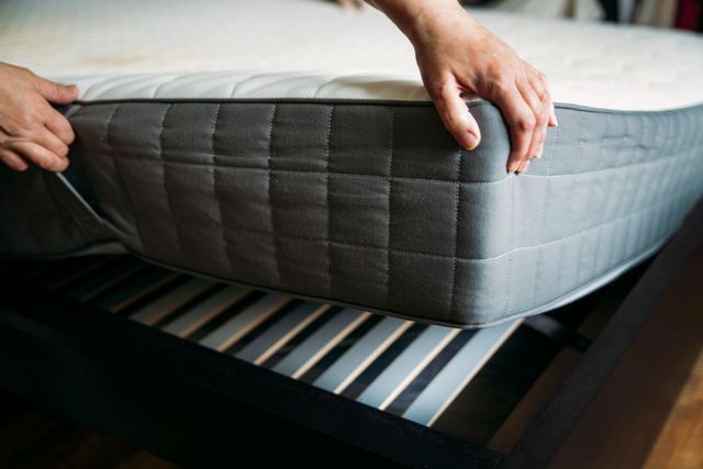 Mani che sistemano un materasso grigio su una struttura letto con doghe di legno.