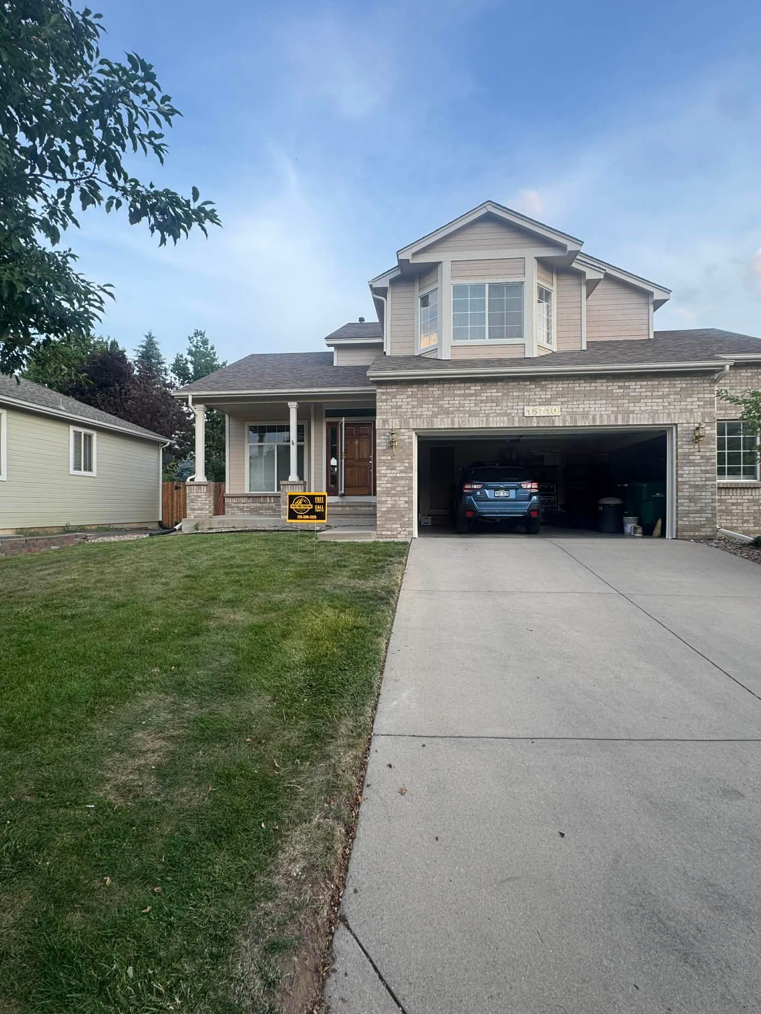 Suburban two-story house with stone facade, open garage, and driveway leading to the street.