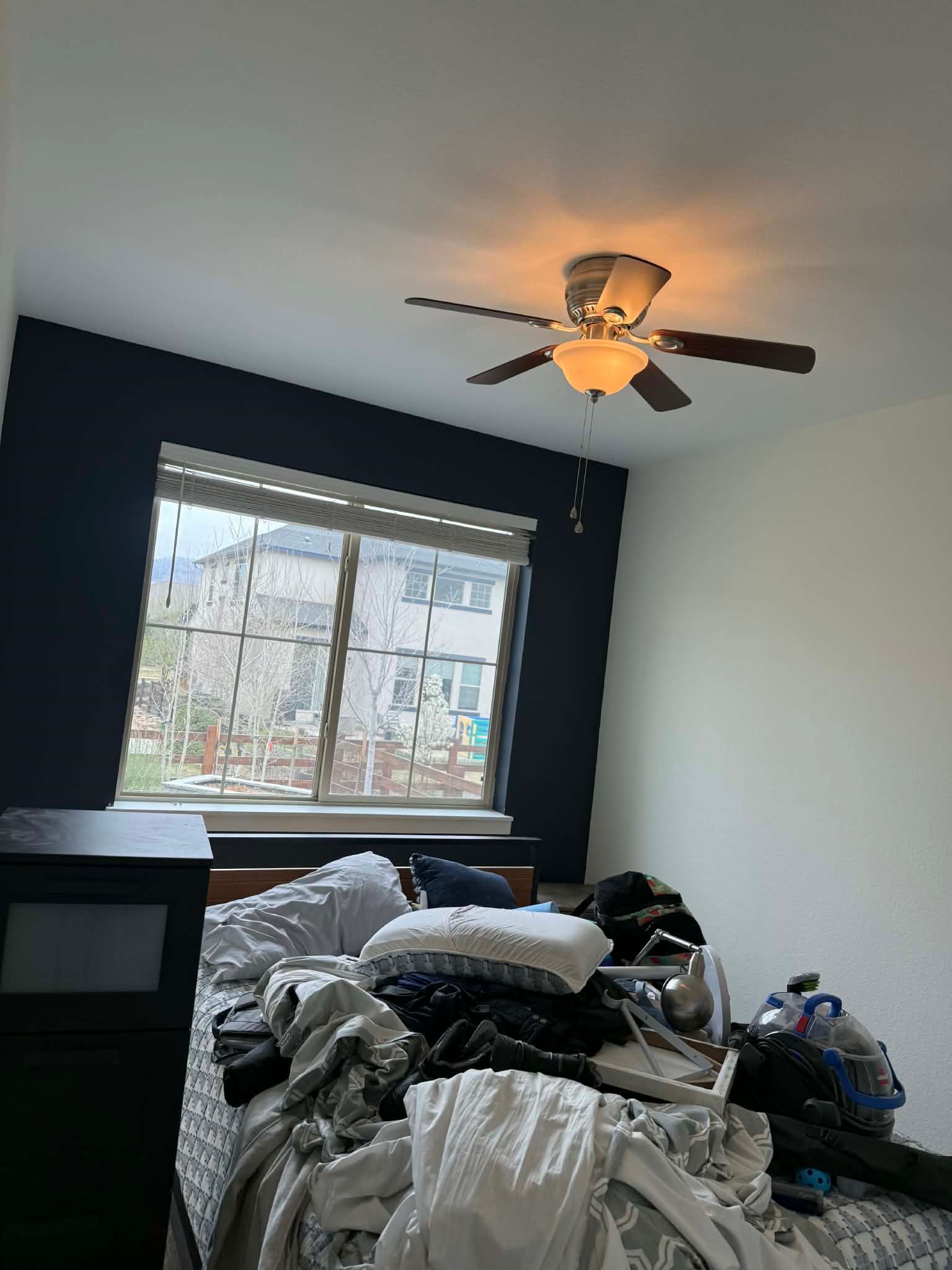 Bedroom with a dark navy accent wall, white walls, and a ceiling fan over a bed piled with blankets and items.