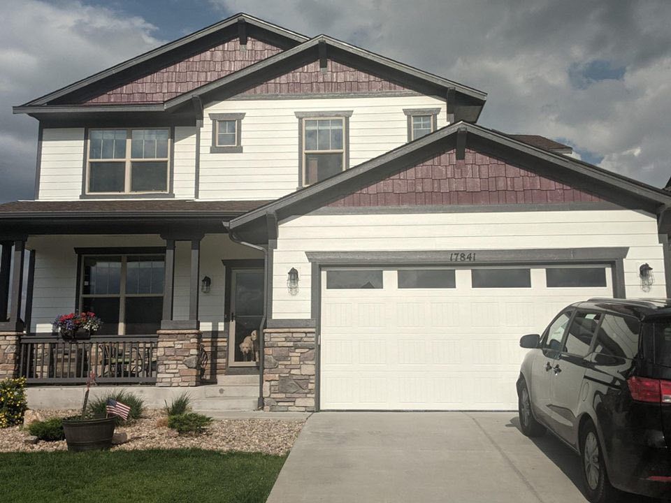 A two-story house with white horizontal siding, dark wood accents, stone trim, a front porch, and a two-car garage.