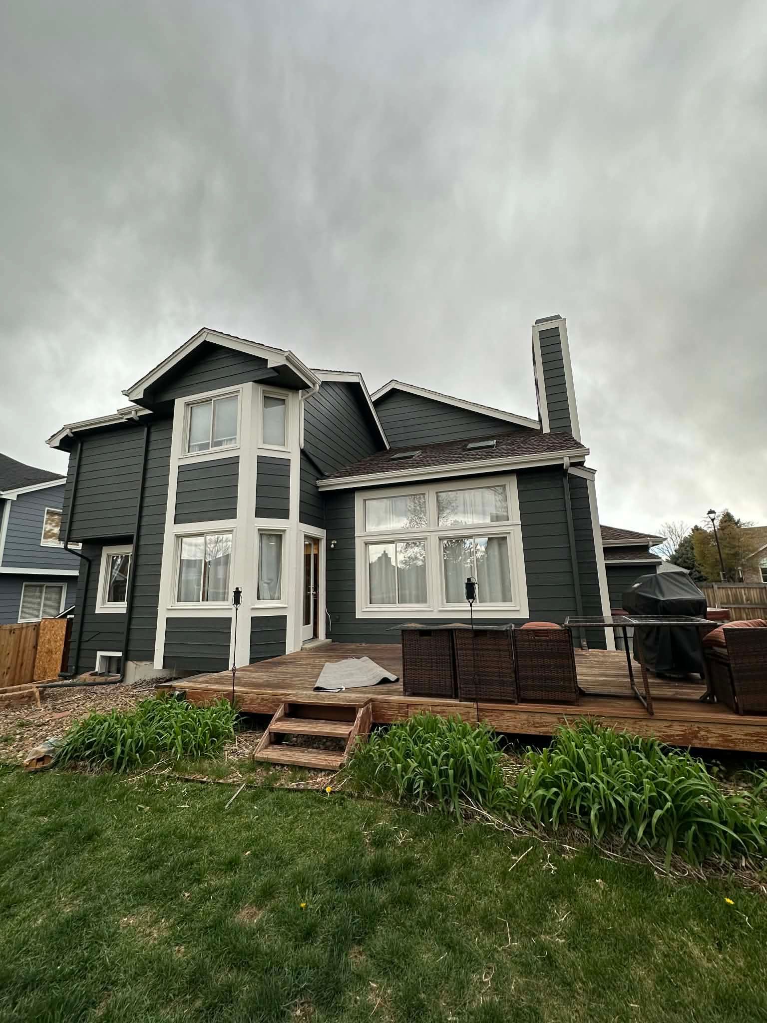 Gray two-story house with white trim and boarded windows under an overcast sky
