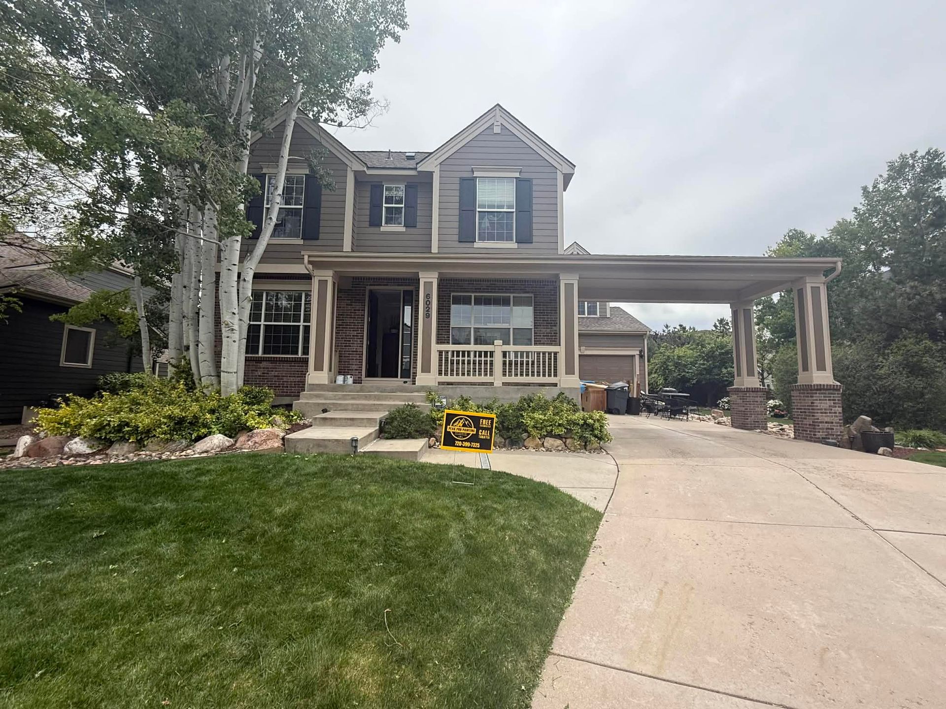 Two-story suburban house with stone porch, front lawn, and driveway under a cloudy sky