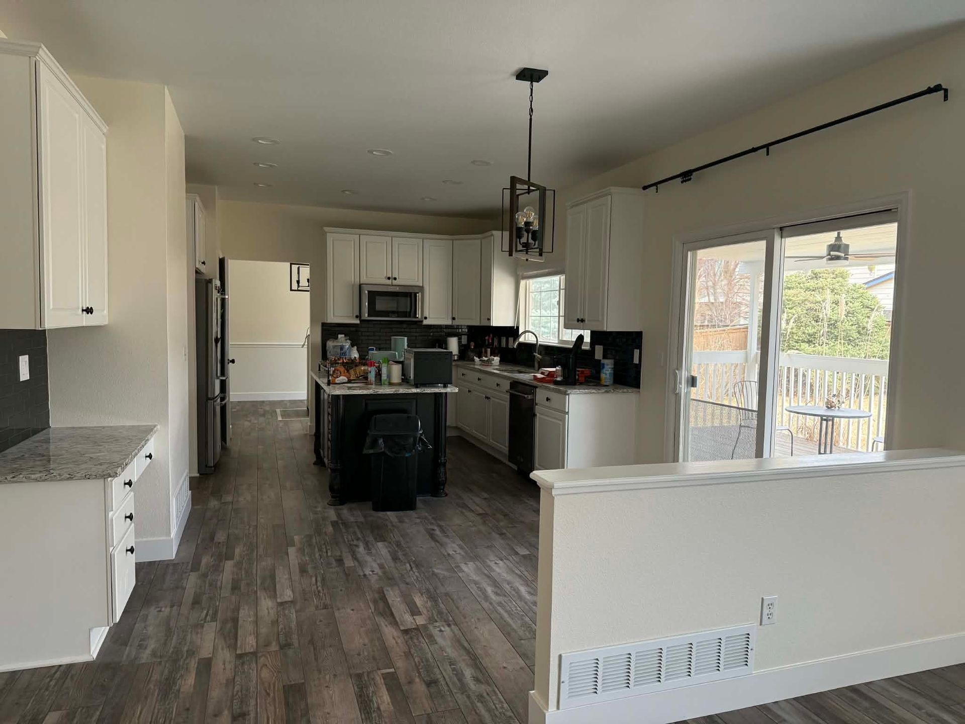 A bright kitchen with white cabinets, a dark island, granite countertops, and wood-patterned flooring.