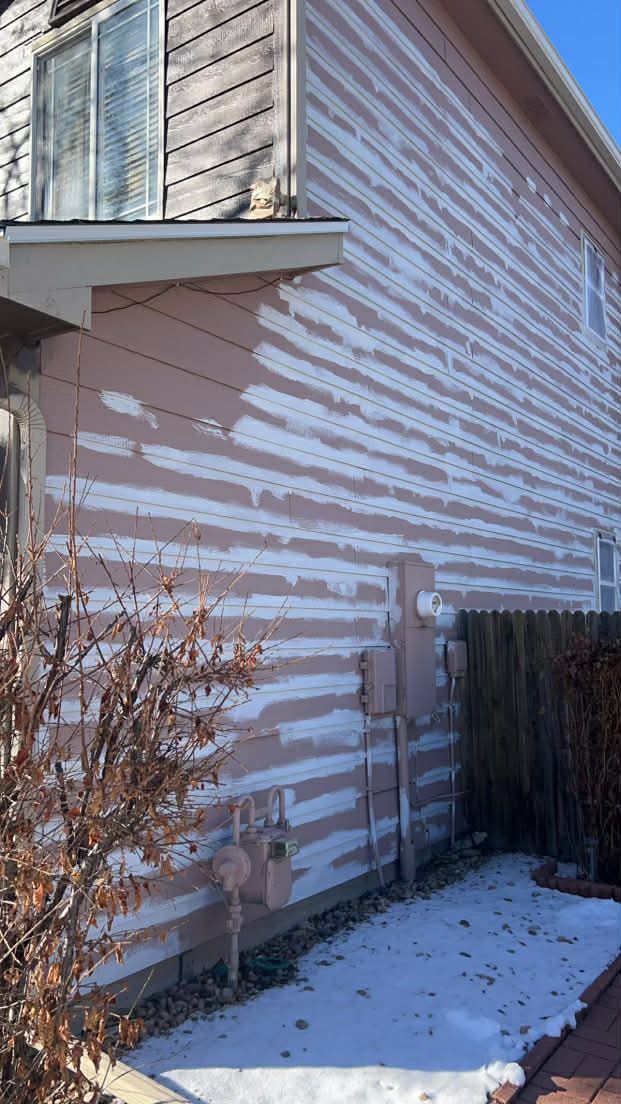 Exterior wall of a house with weathered, peeling pink paint revealing white substrate beneath.