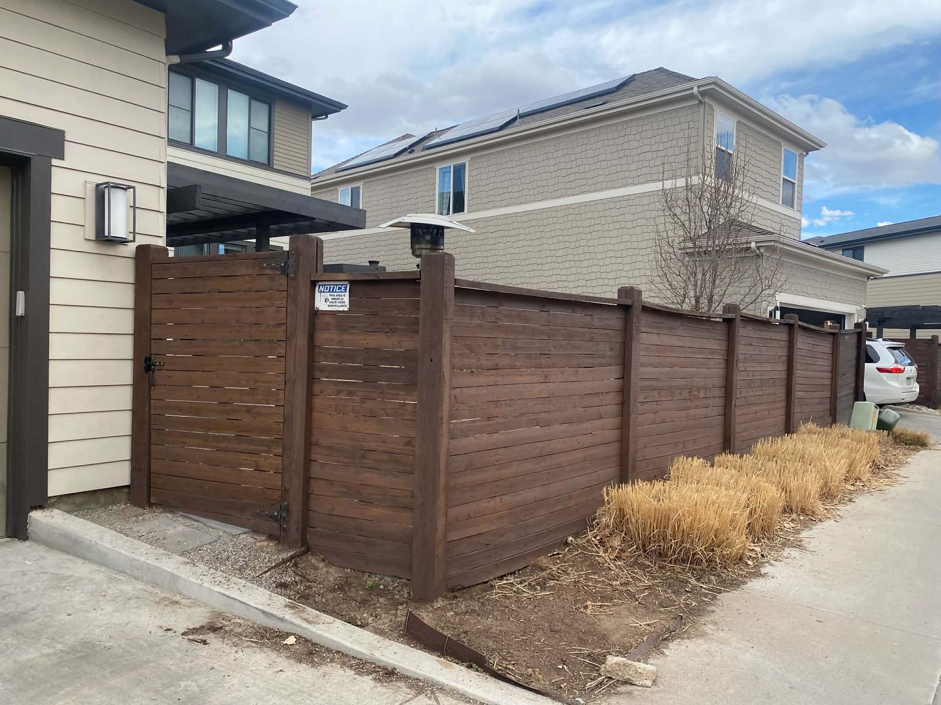 A brown horizontal-slat wooden fence enclosing a small outdoor space next to a modern suburban house.