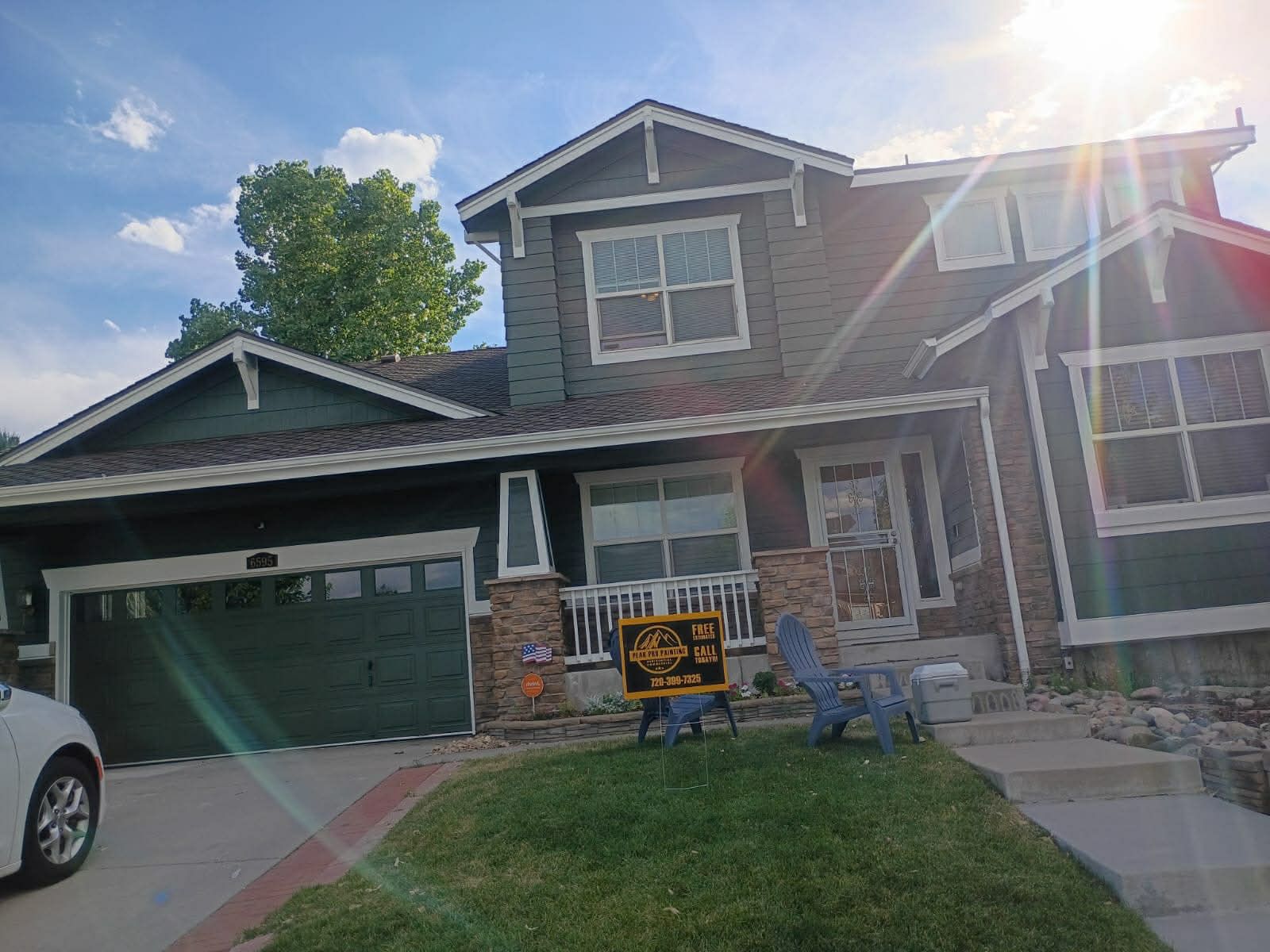 Two-story suburban house with green garage door, front lawn, and bright sun glare