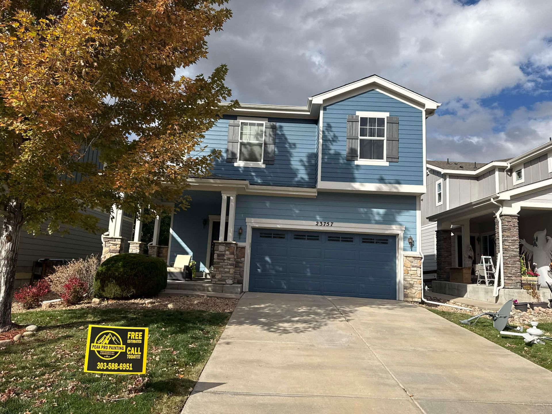 Blue two-story suburban house with a garage, driveway, and autumn tree in front