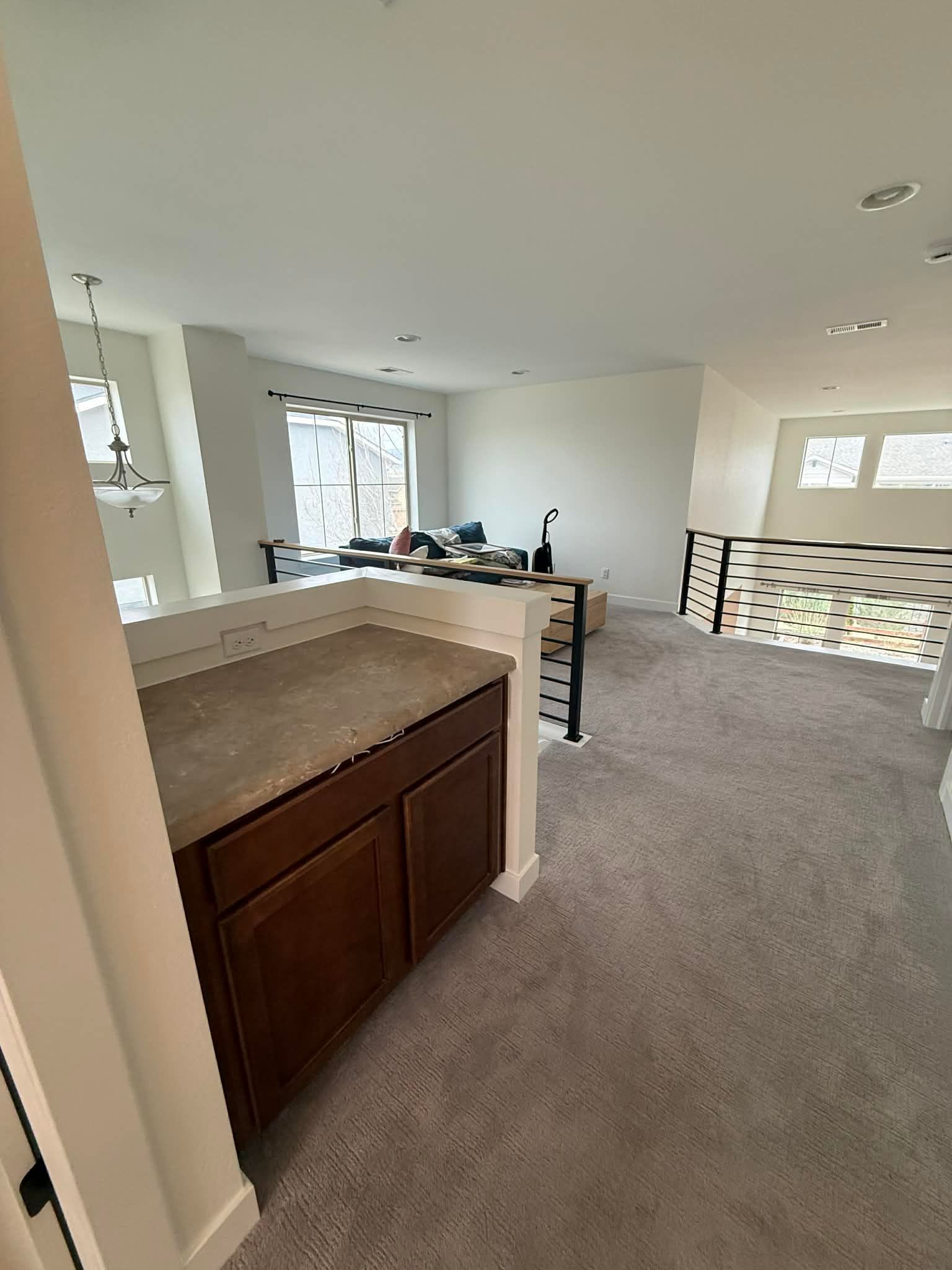 A loft area featuring a wet bar with dark cabinets and a granite countertop, carpeted flooring, and a metal railing.