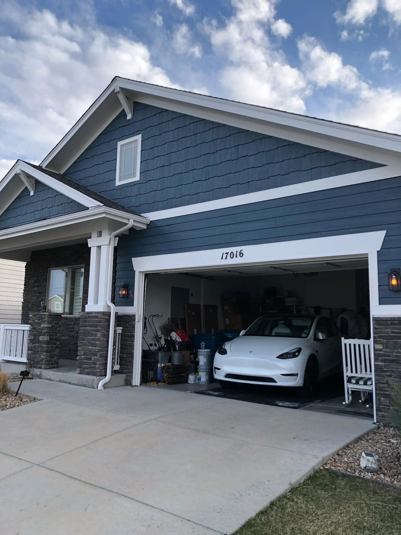 Blue house with open garage, a white sports car parked inside, and a cloudy sky overhead
