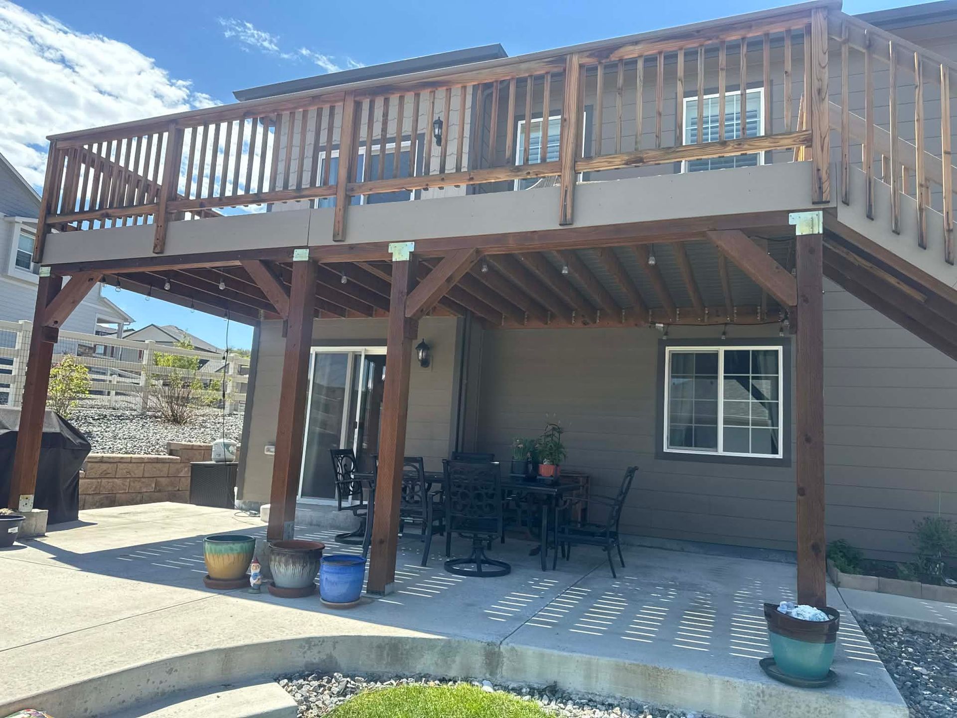Wooden deck with railing and patio furniture over a shaded ground-level patio beside a house