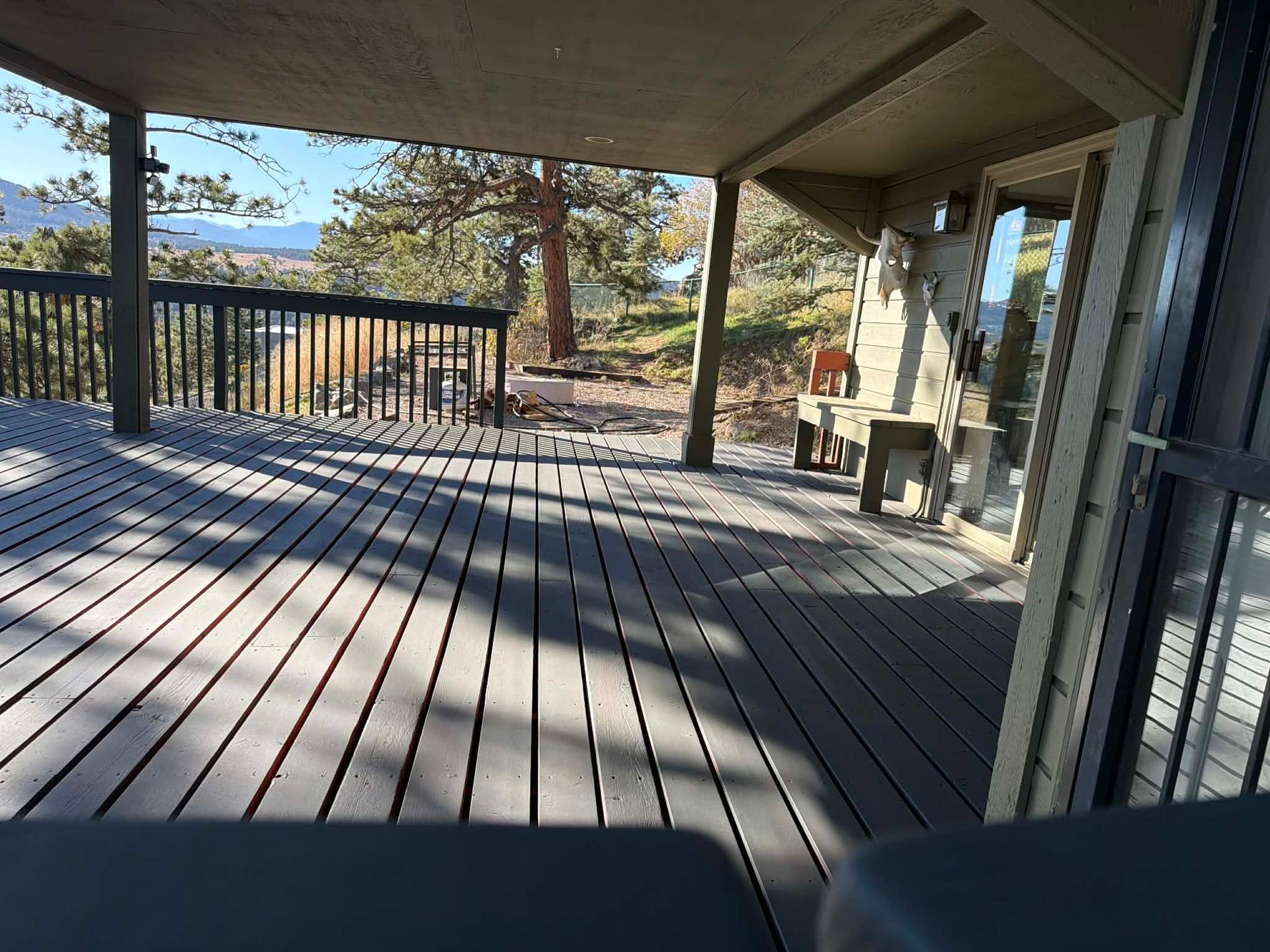 Covered wooden deck with railing, black chair, and outdoor view of trees and hills