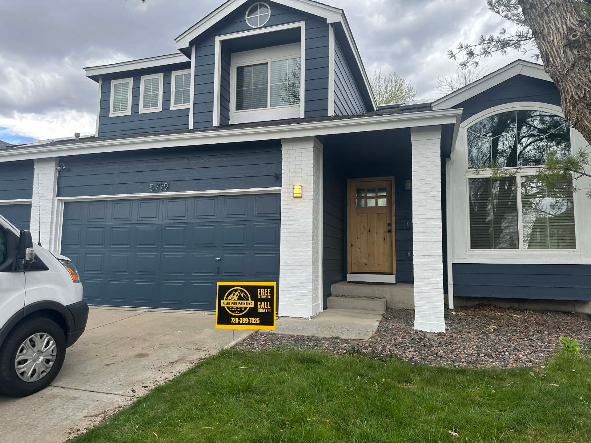 Blue-gray house with a black garage door and a yard sign in front of the driveway.