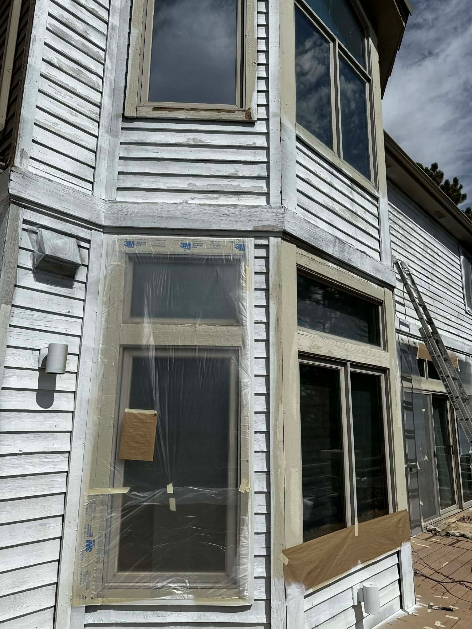 A two-story building exterior under renovation with white siding, dark window frames, and protective construction paper.