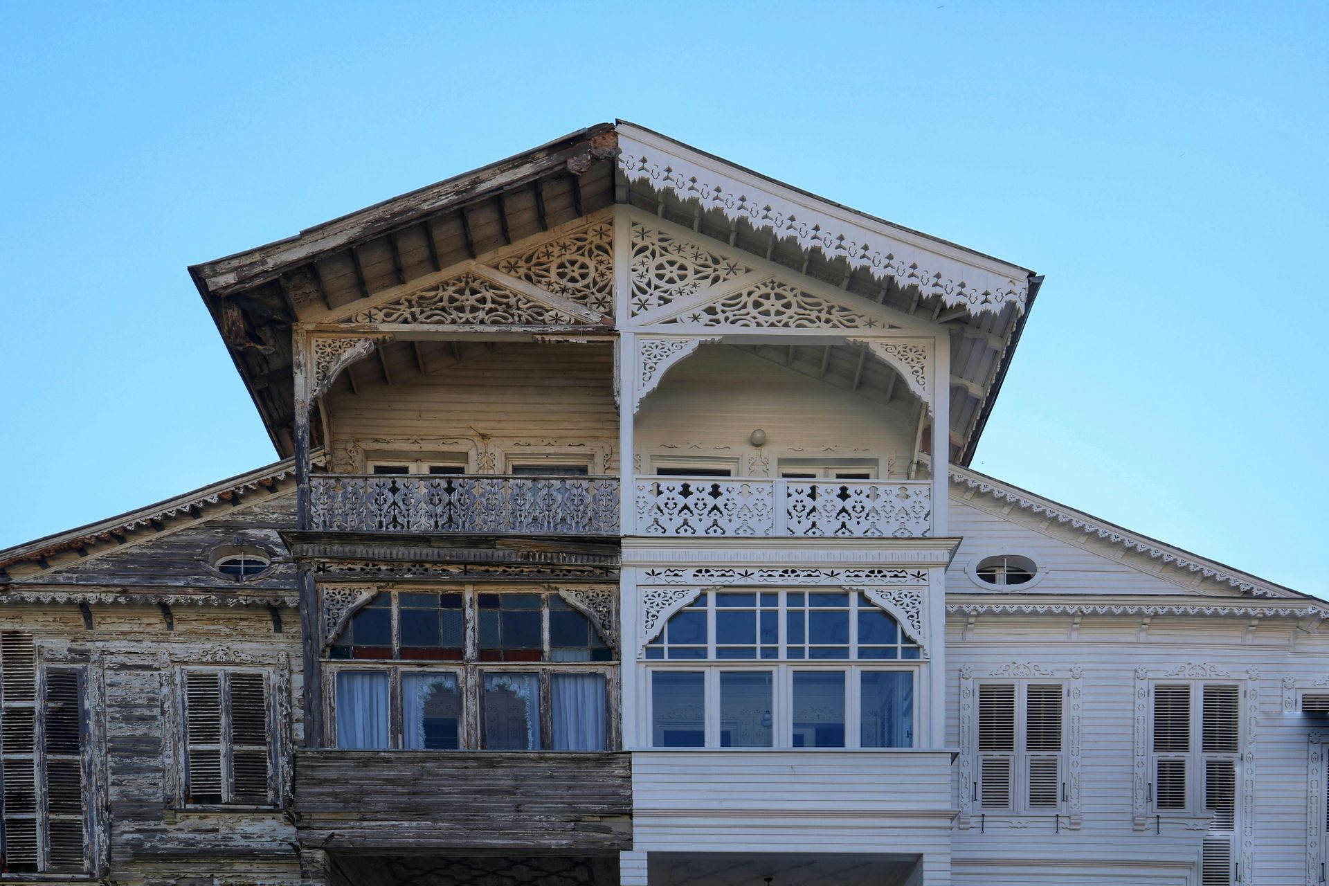 A historic wooden building featuring a striking contrast between a weathered, dark side and a freshly painted white side.