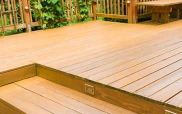 A wooden deck with a built-in step light, railing, and bench in an outdoor garden setting.