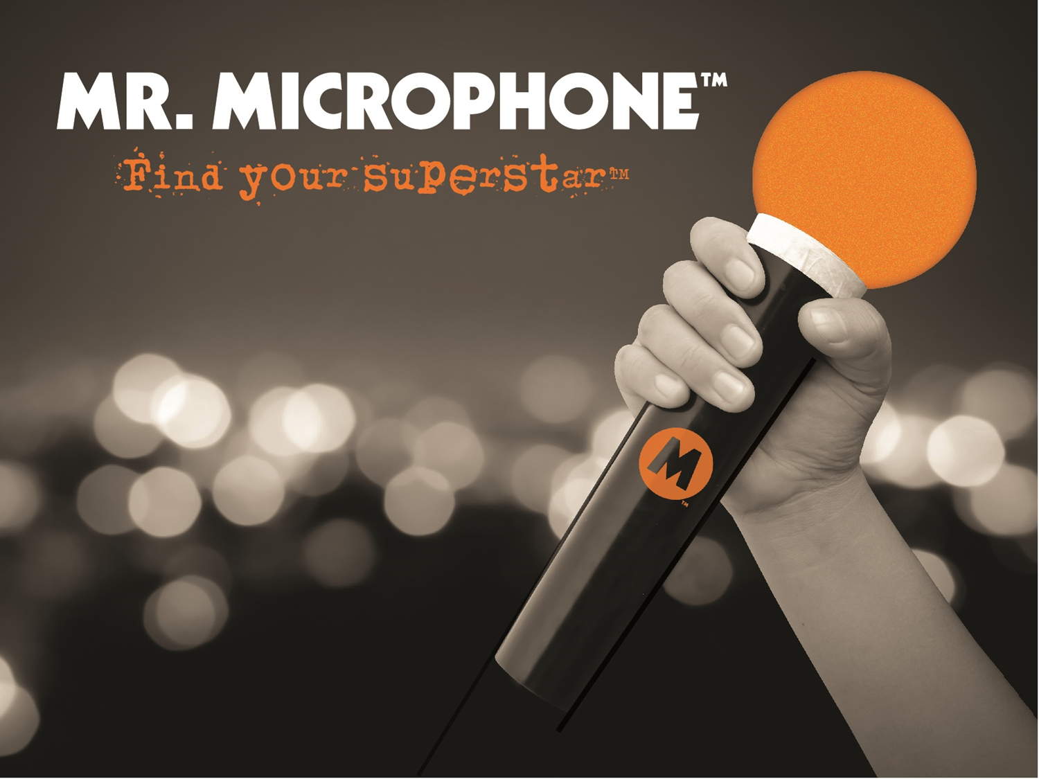 A hand holds a black Mr. Microphone with an orange foam cover against a blurry, bokeh-lit background.