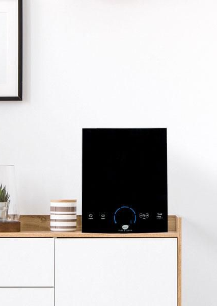 Black square speaker on a wooden cabinet in a bright minimalist room.