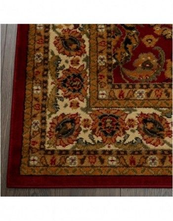 A red and gold rug with a floral pattern is on a wooden floor.